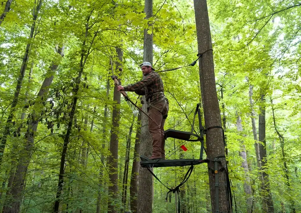 A person standing at a tree stand preparing to aim