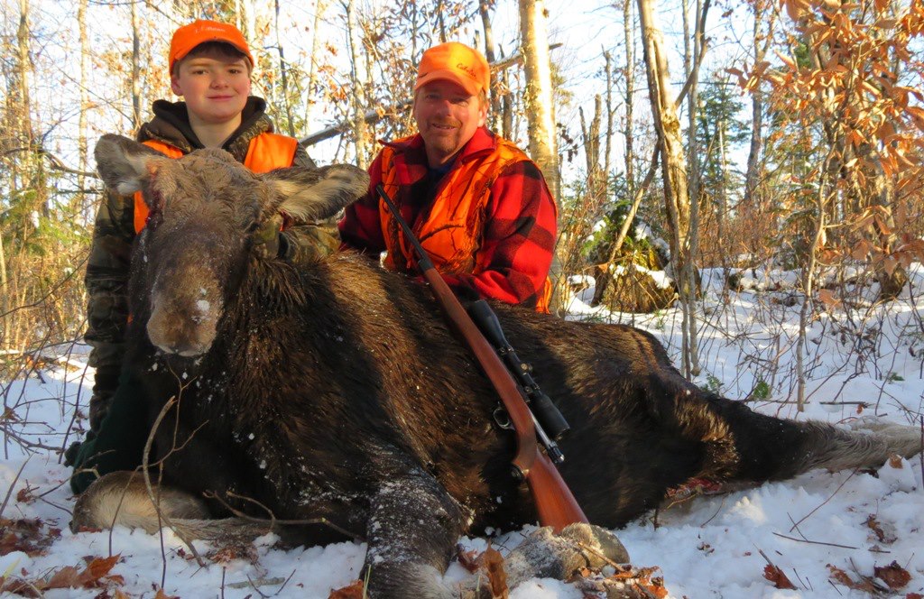 A view of a kid and a hunter with a Moose sitting in snow