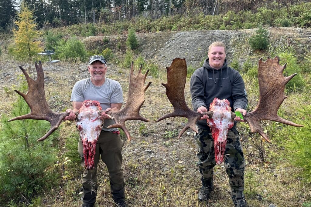 A view of two guys standing with a hunted Moose's horns