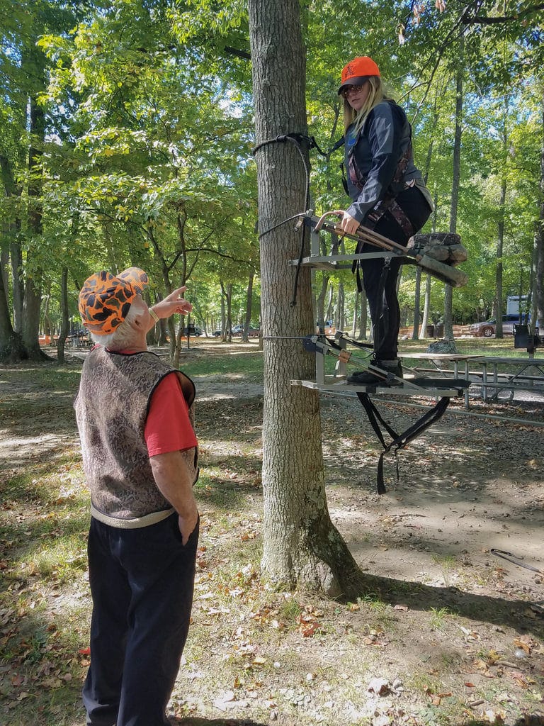 An old man instructing a girl putting up a tree stand