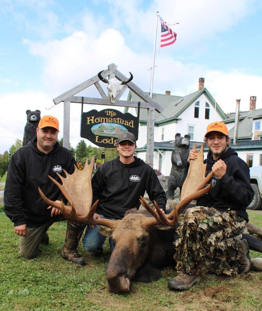 Three hunters sitting in front of the homestead lodge holding a dead moose deers horns for hunting