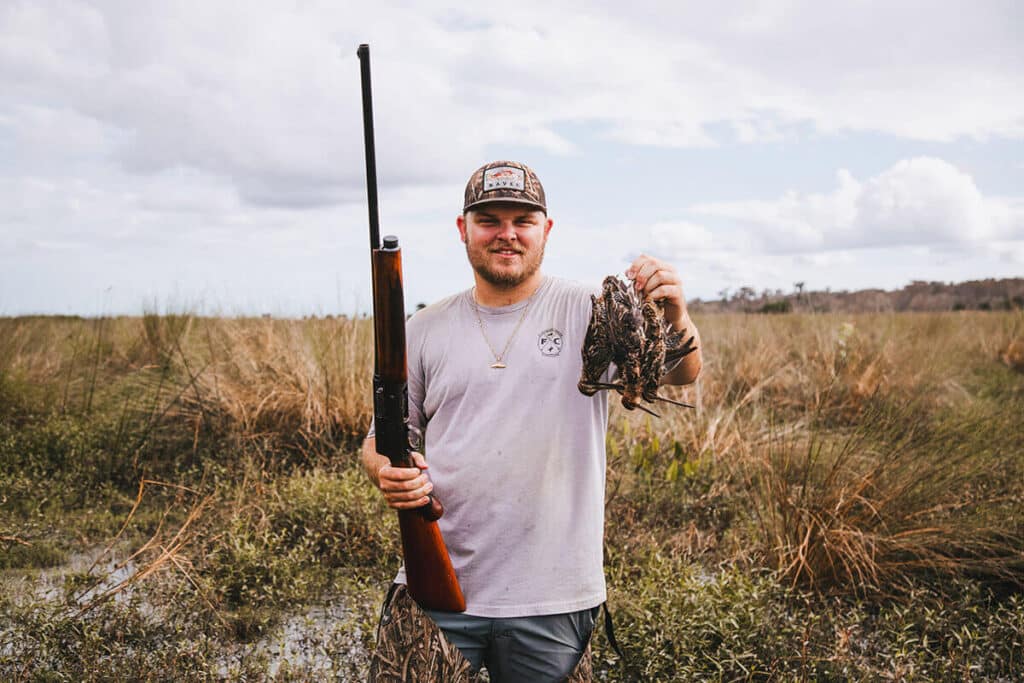 hunter holding a snipe and a gun in an open land