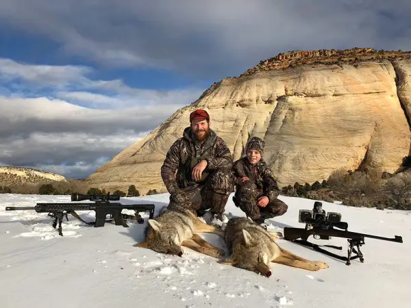 a hunter with his son along with the dead coyote and shooting guns in snow