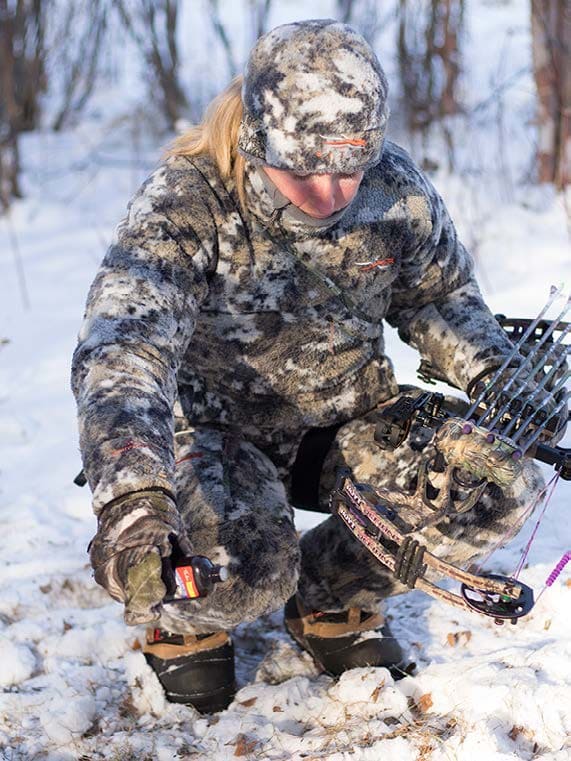 a women in cold snowy place and wearing winter hunting suit