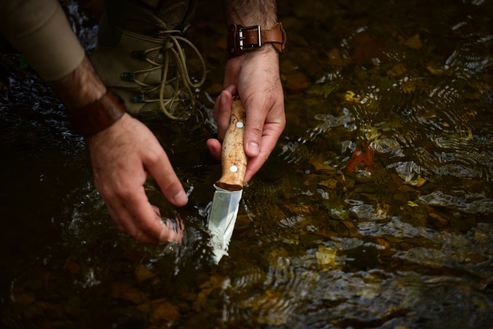 A Hunter Washing His Knife In A Flowing Stream